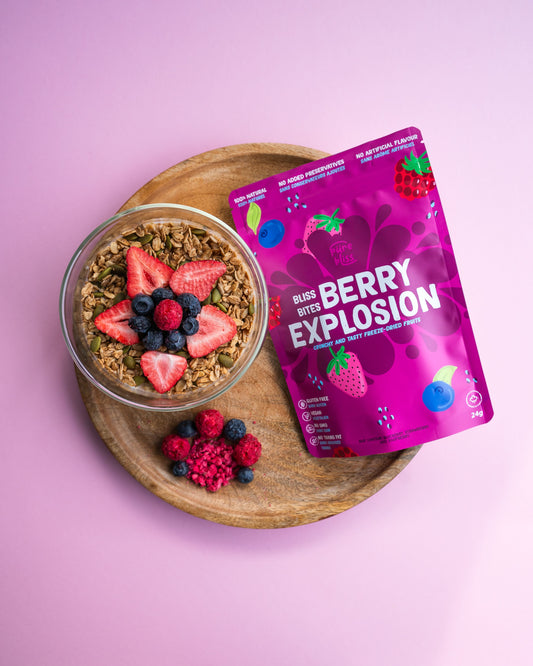 Bowl of granola with freeze dried berries and a package of 'Berry Explosion' on a pink background