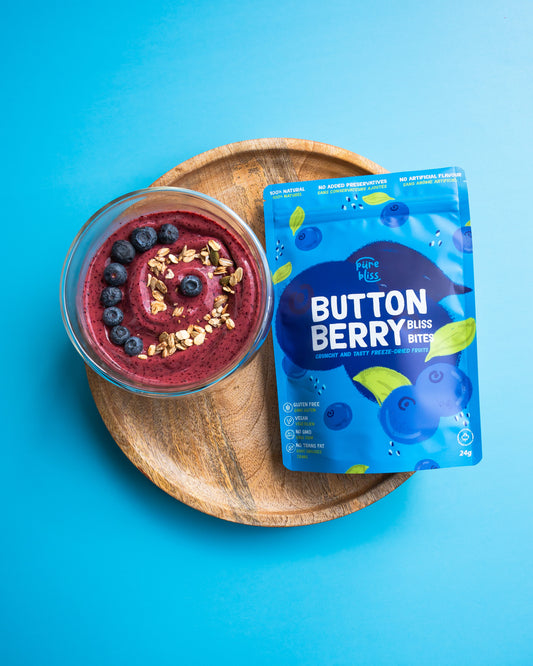 Berry smoothie with granola on a wooden plate next to a package of Button Berry bliss bites on a blue background