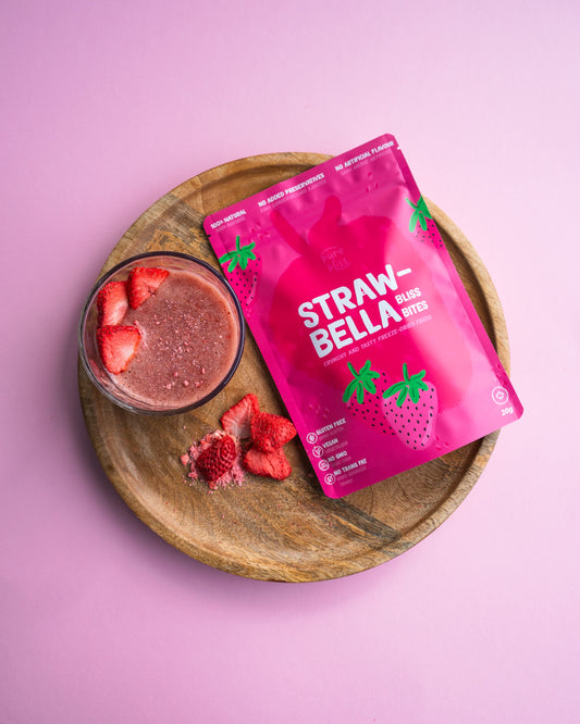 Package of StrawBella on a wooden board beside a smoothie and strawberries on a pink background