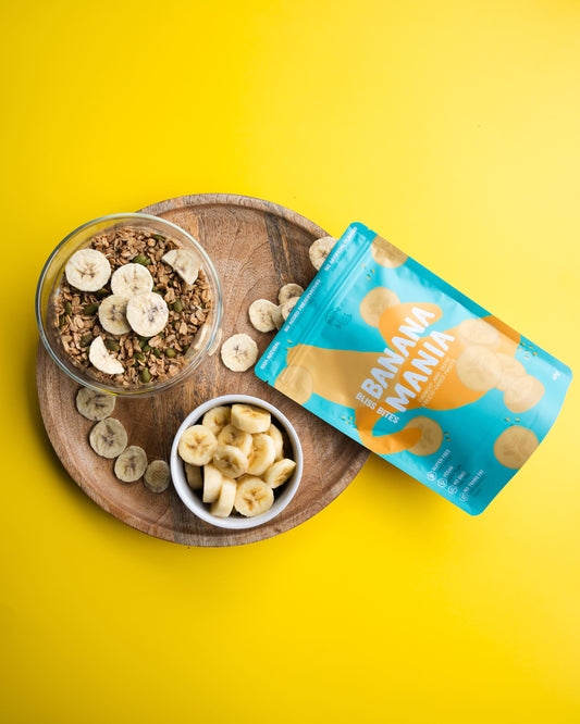 Banana freeze dried chips packaging with a wooden tray of banana slices and granola on a yellow background