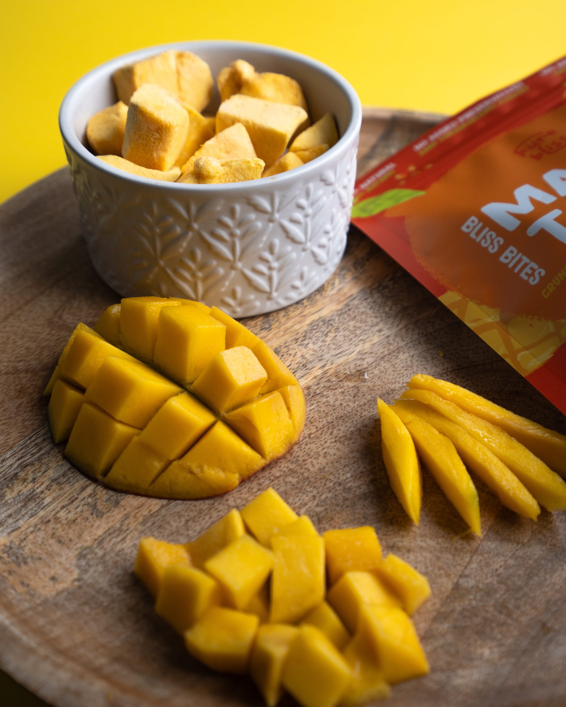 Mango bites in a white bowl on a wooden surface with a yellow background