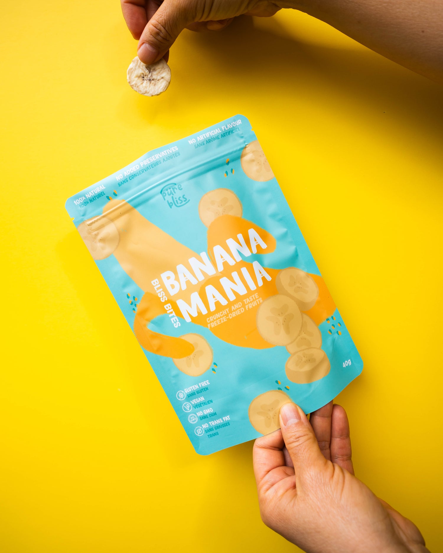 Hand holding a packet of 'Banana Mania' snacks on a yellow background