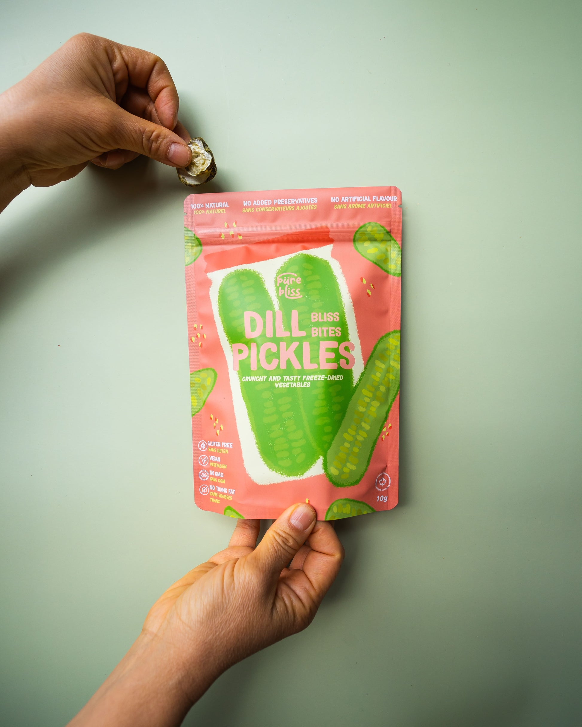 Hand holding a pink package of dill pickles against a light green background