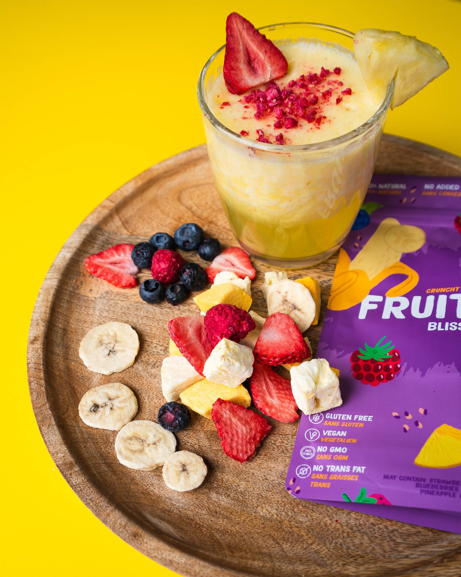 Fruit smoothie with toppings on a wooden tray next to a package of Fruity Bliss.
