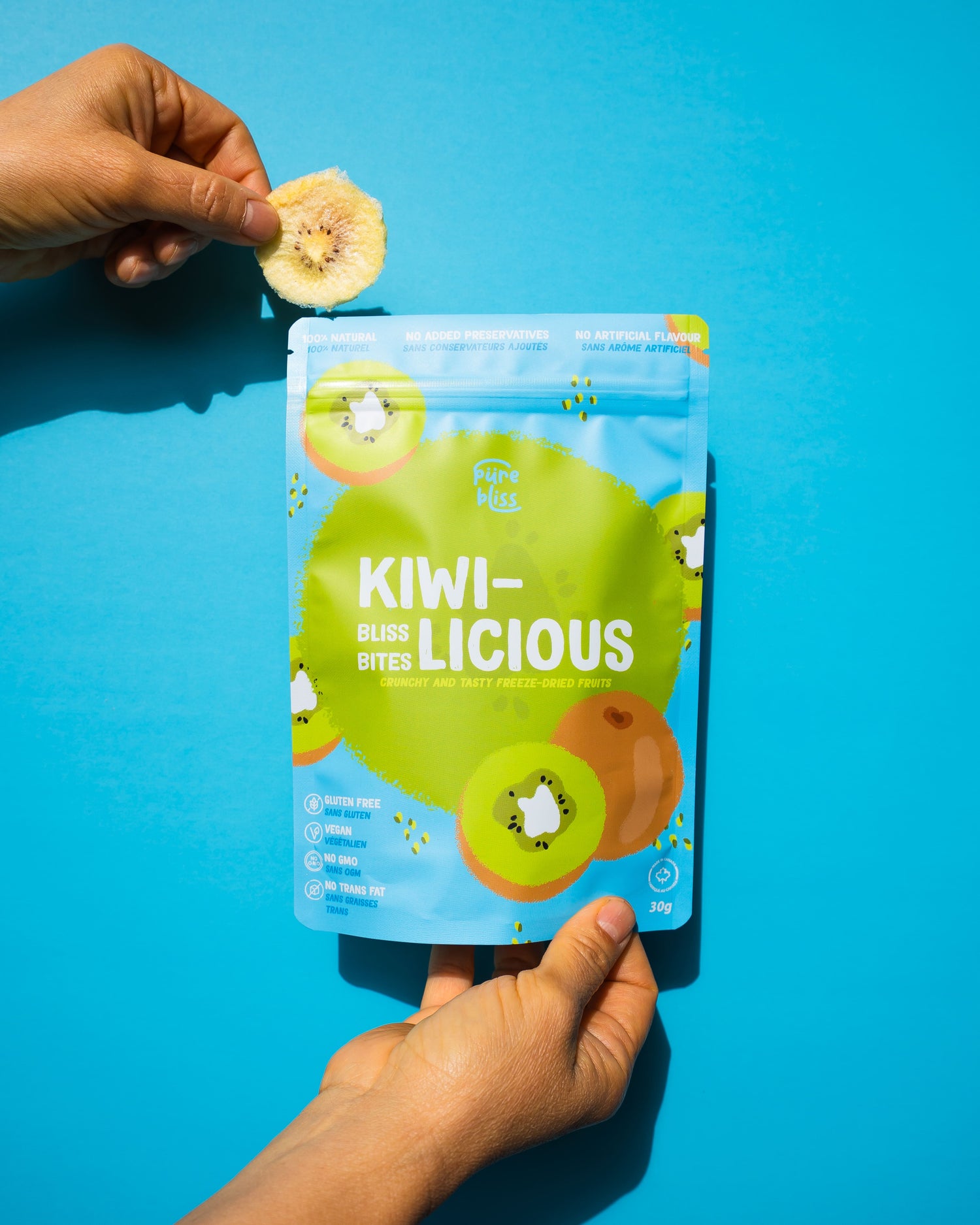 Hand holding a packet of 'Kiwi-licious' bites against a blue background
