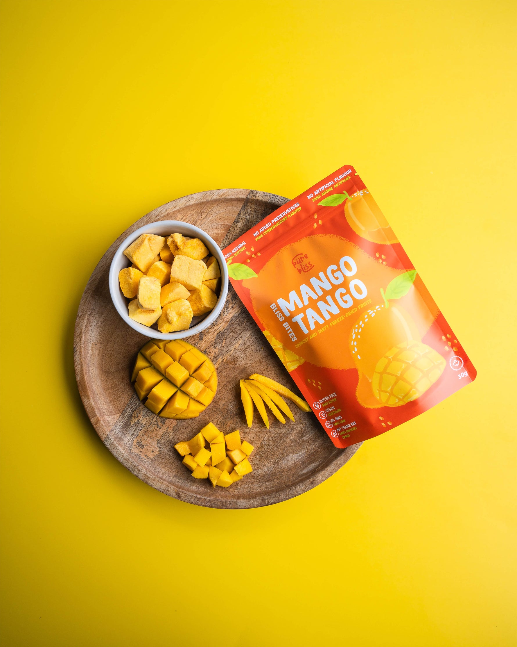 Freeze dried mango bites on a wooden tray with a 'Mango Tango' package against a yellow background