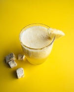Glass of creamy pineapple juice, with a slice of pineapple on a yellow background