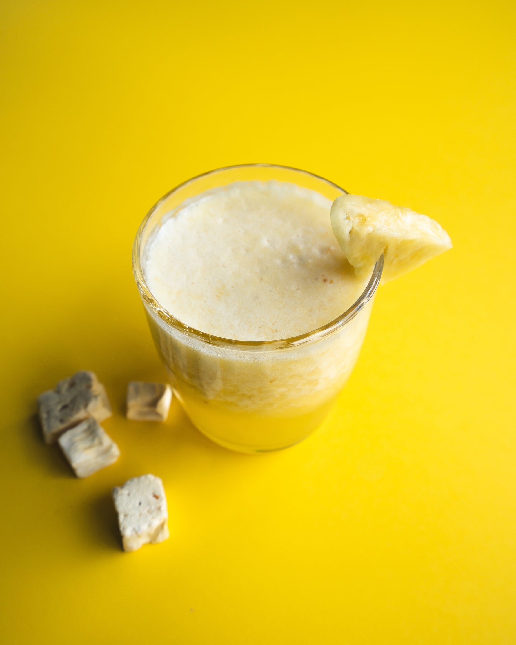 Glass of creamy pineapple juice, with a slice of pineapple on a yellow background