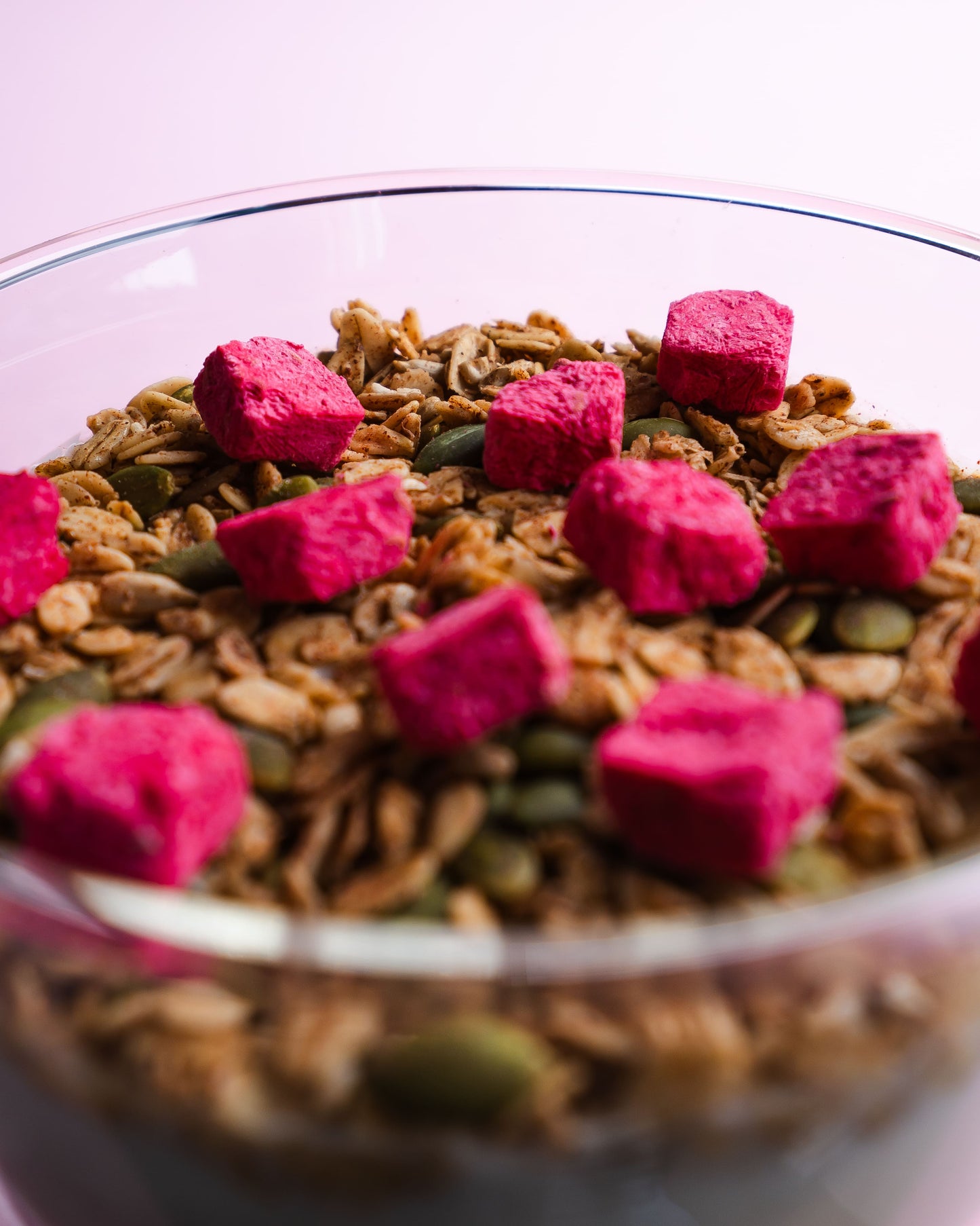 Glass bowl filled with granola and pink powder on a light purple background