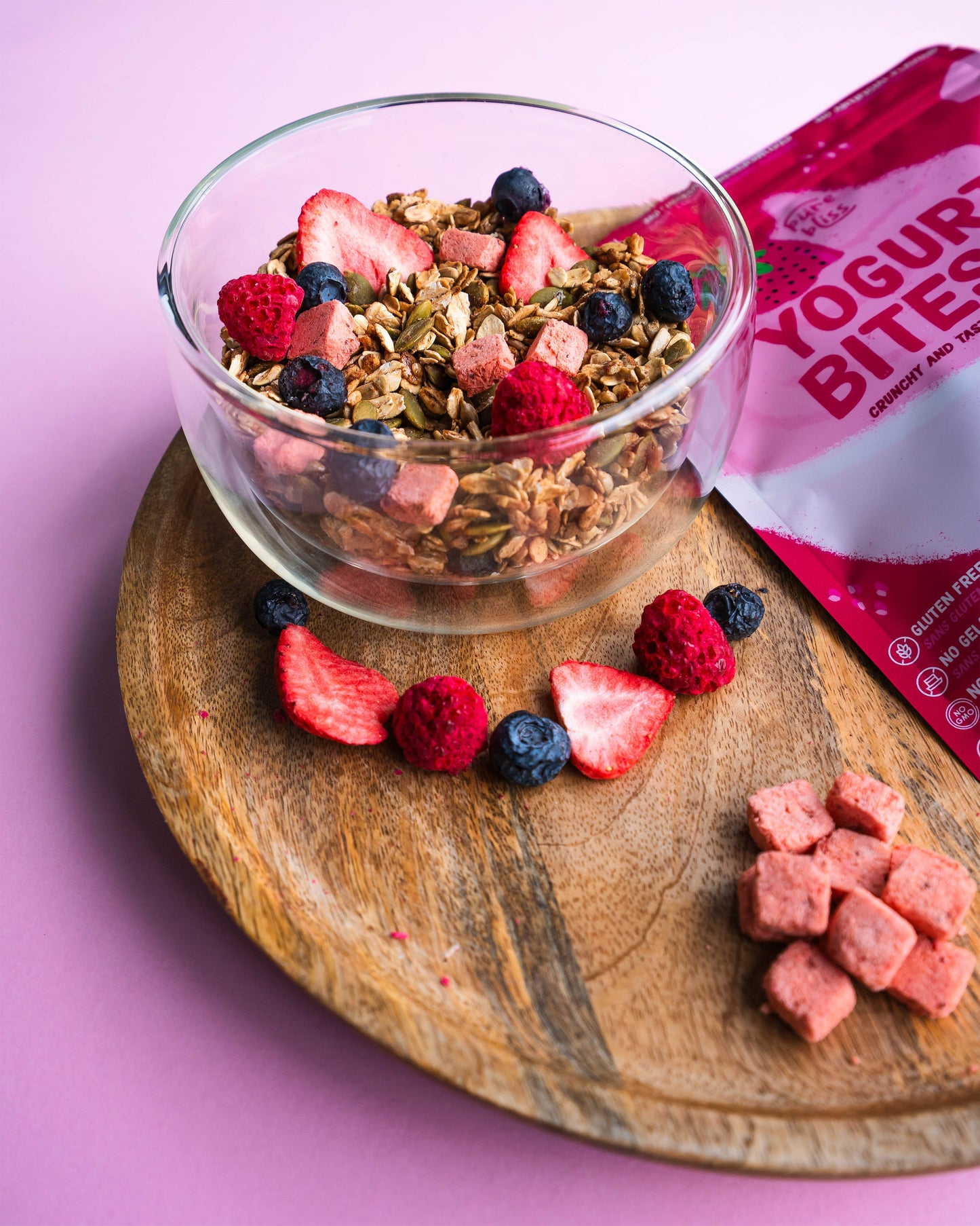Glass bowl with granola and berries on a wooden board with yogurt bites packaging in the background