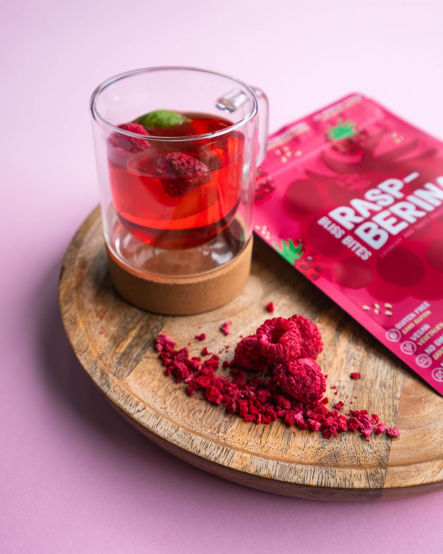 Glass of raspberry tea with a wooden coaster on a pink background